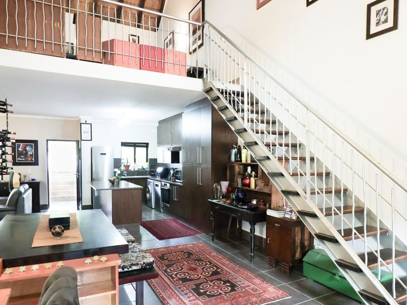 Spacious open-plan living area featuring a modern kitchen, a central island, and a staircase leading to a mezzanine level with timber ceiling beams.