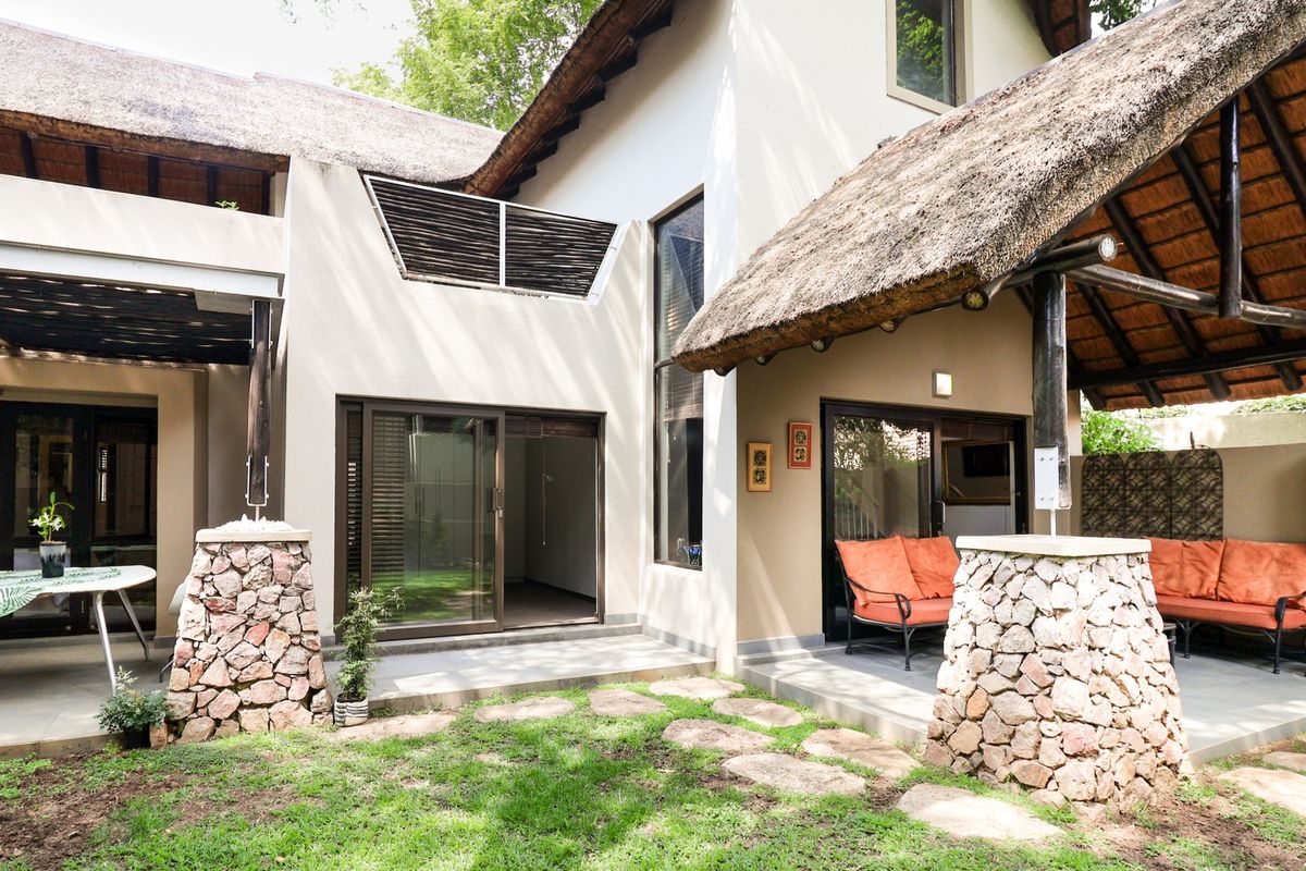 Rear exterior view of a townhouse featuring a thatched roof, stone-clad pillars, and a paved patio area leading to a garden.