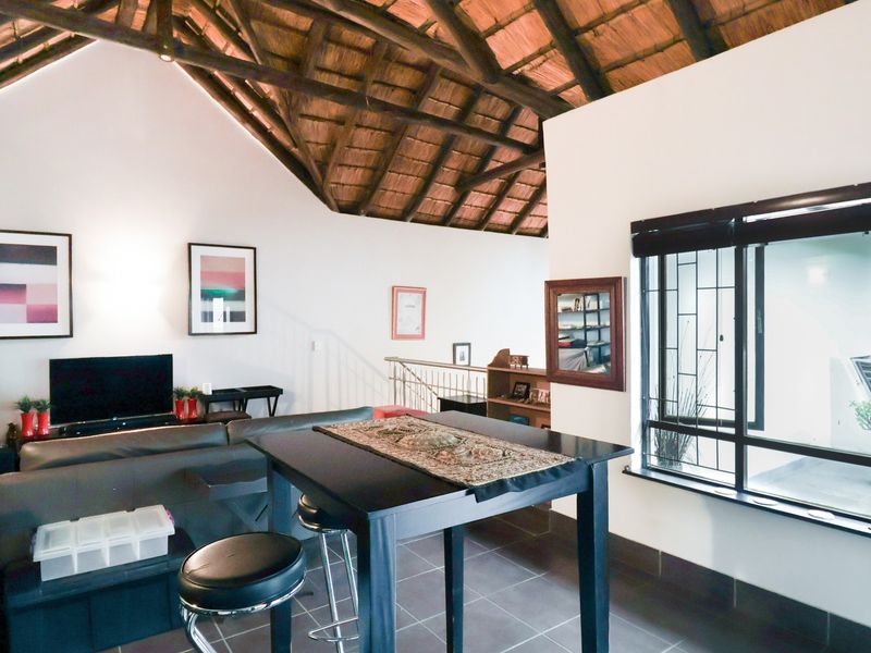 Open plan living area featuring high vaulted ceilings with exposed timber rafters, thatched roof finish, and large windows with security bars.