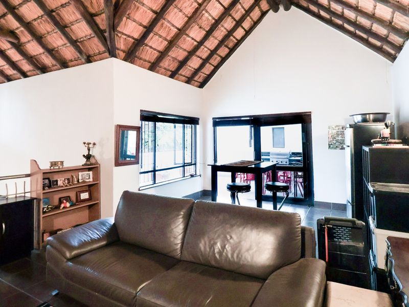 Spacious living area featuring a high vaulted ceiling with exposed thatch roofing, tiled floors, and direct access to an outdoor patio area.