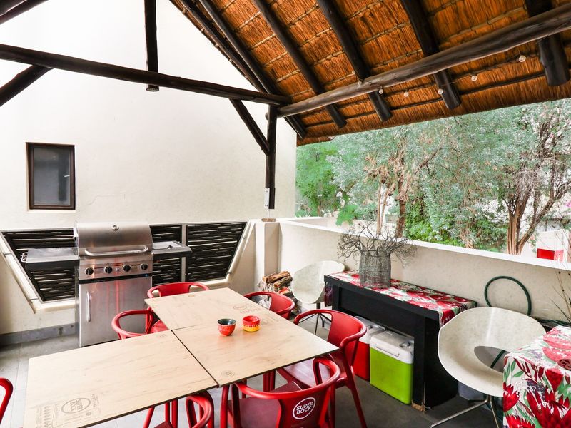 Covered patio area featuring a traditional thatched roof, exposed timber beams, and a built-in braai, perfect for outdoor entertaining.