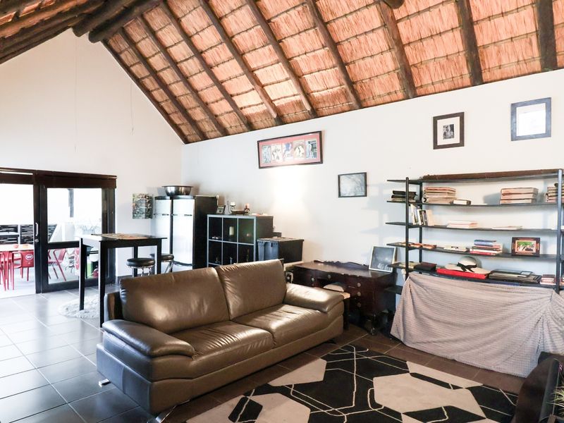 Spacious living area featuring a high vaulted thatched ceiling with exposed timber rafters and tiled flooring, leading out to a patio.