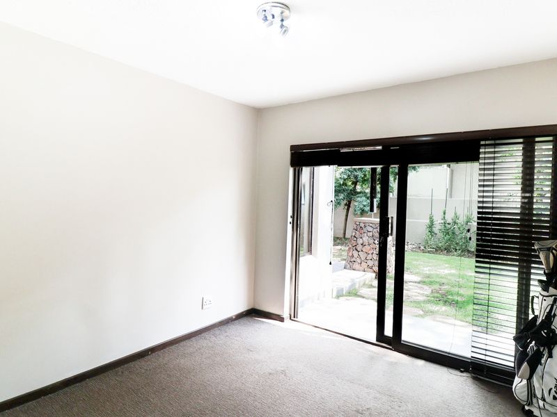 An empty living room featuring neutral walls, carpet flooring, and a large sliding glass door providing direct access to the rear garden.