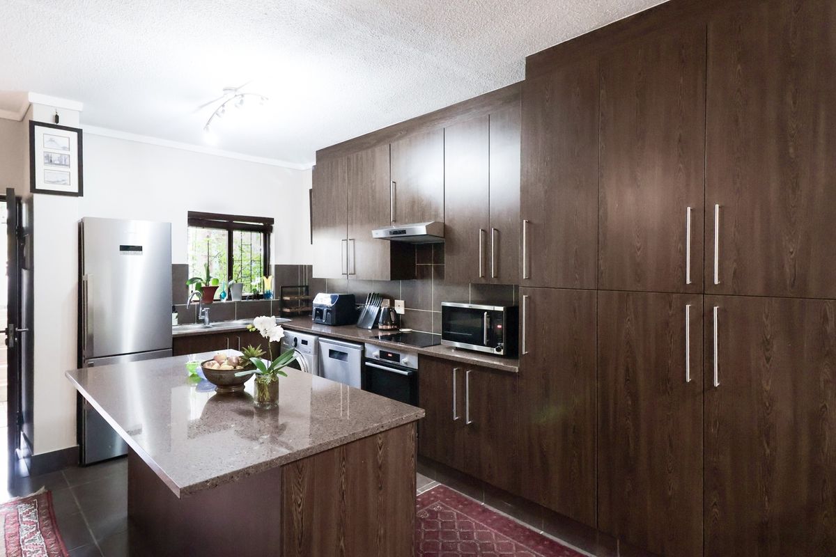 Modern kitchen featuring dark wood cabinetry, stone countertops, a central island, and integrated appliances, offering a functional and stylish cooking space.