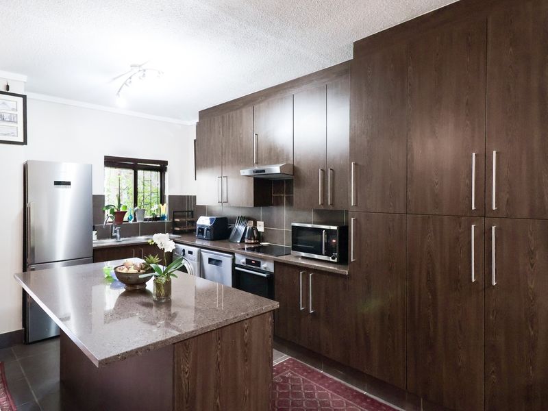 Modern kitchen featuring dark wood cabinetry, stone countertops, a central island, and integrated appliances, offering a functional and stylish cooking space.