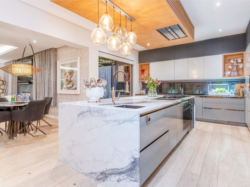 Modern open-plan kitchen featuring a marble island, high-end built-in appliances, timber ceiling accents, and premium hardwood flooring in a sophisticated, well-lit space.