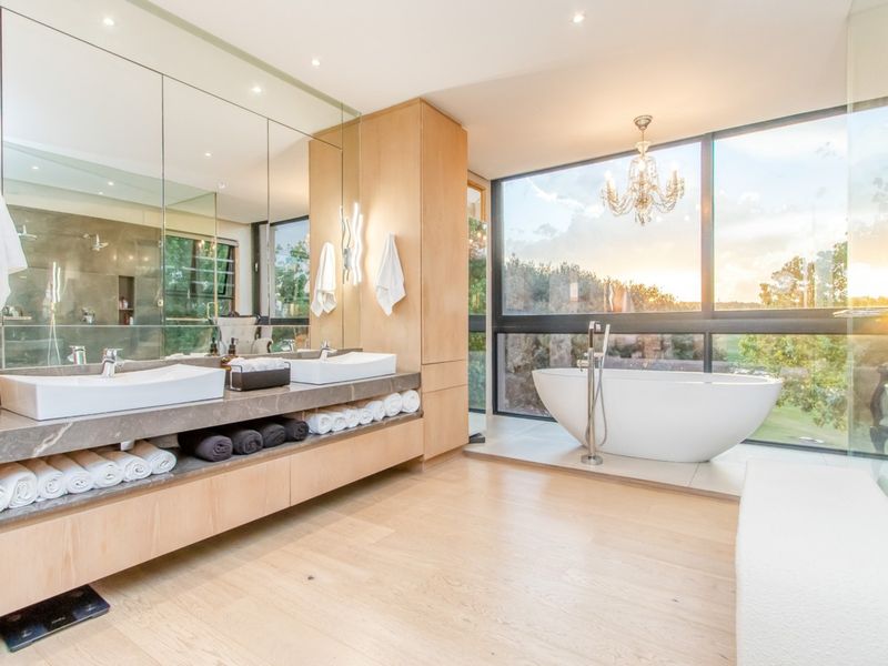 Luxurious modern bathroom featuring a double vanity with stone countertop, freestanding bathtub, and expansive floor-to-ceiling windows offering scenic views.