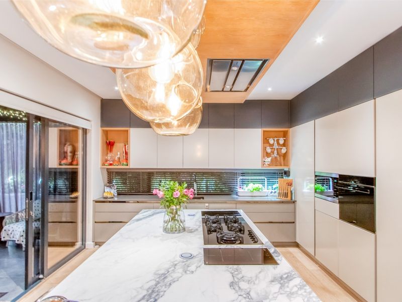Modern kitchen featuring a marble island with integrated gas hob, sleek cabinetry, built-in appliances, and large sliding doors opening to an outdoor area.