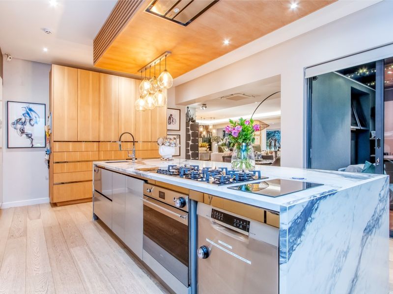 Modern kitchen featuring a large marble island with integrated gas cooktop, high-end built-in appliances, custom wooden cabinetry, and elegant recessed lighting.