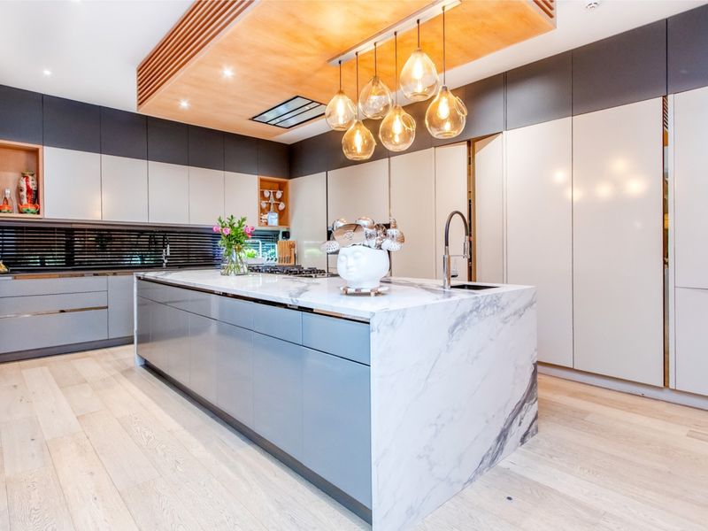 Modern luxury kitchen featuring a large marble waterfall island, sleek integrated cabinetry, high-end finishes, and a stylish recessed ceiling detail with pendant lighting.