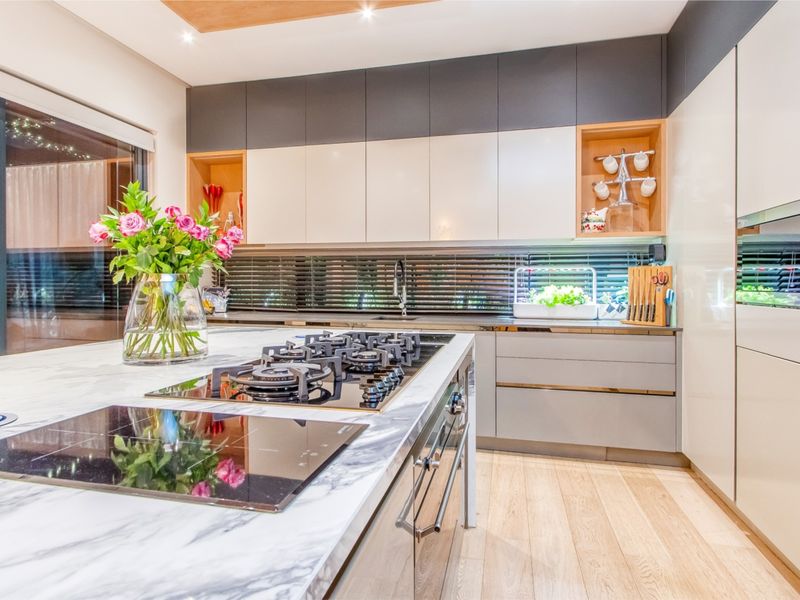 Modern kitchen featuring a marble-look island with dual cooktops, sleek integrated cabinetry, recessed shelving, and high-quality hardwood flooring.
