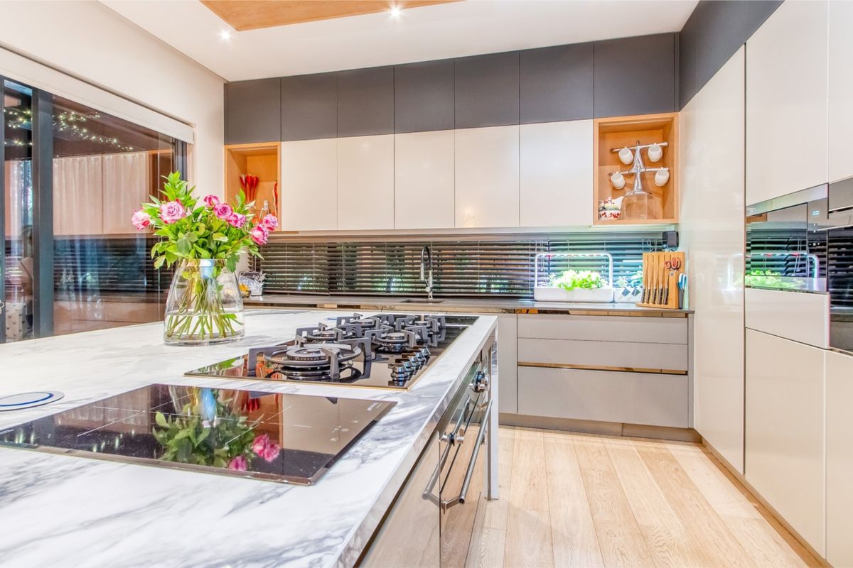 Modern kitchen featuring a marble-look island with dual cooktops, sleek integrated cabinetry, recessed shelving, and high-quality hardwood flooring.