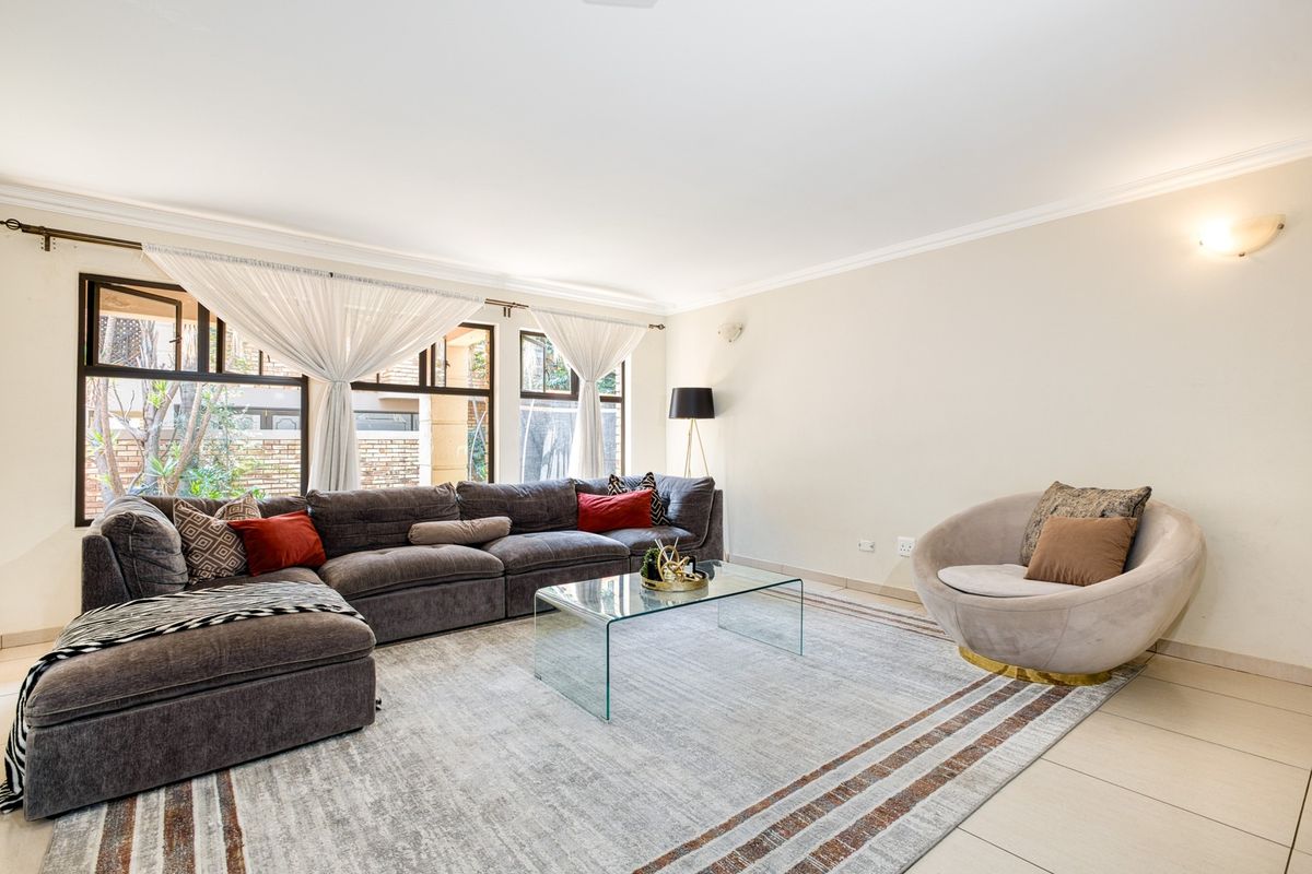 A bright and spacious living room featuring large windows, neutral tiled flooring, and elegant wall-mounted lighting, creating a comfortable and inviting atmosphere.