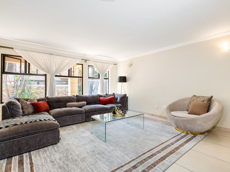 A bright and spacious living room featuring large windows, neutral tiled flooring, and elegant wall-mounted lighting, creating a comfortable and inviting atmosphere.