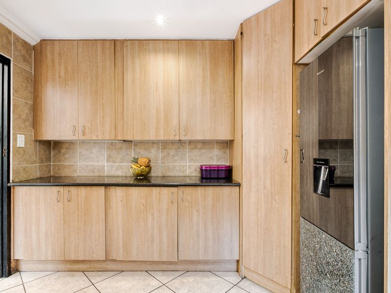 A functional kitchen area featuring light wood-finish cabinetry, dark granite countertops, and neutral tiled backsplash and flooring.
