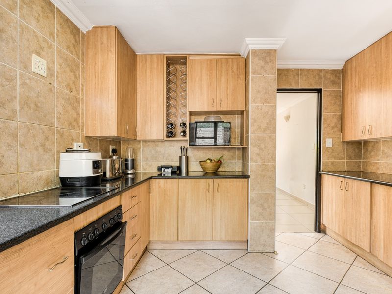 A functional kitchen featuring light wood cabinetry, granite countertops, ceramic tile backsplash, and built-in oven with electric hob.