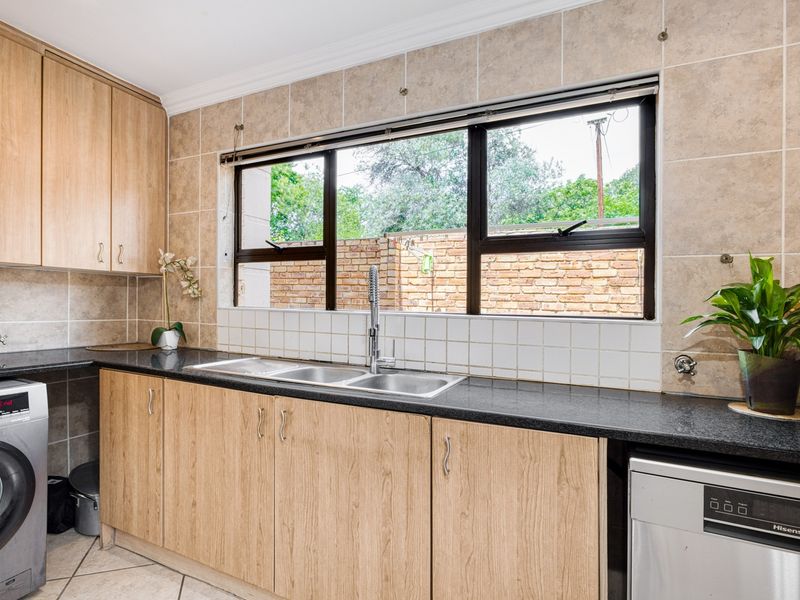 A functional scullery featuring light wood cabinetry, granite countertops, a double basin sink, and tiled finishes, providing ample space for laundry and kitchen prep.