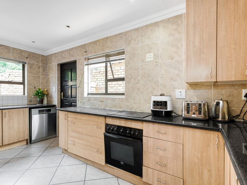 A functional kitchen featuring light wood cabinetry, dark granite countertops, a built-in oven and hob, and neutral tiled finishes throughout.