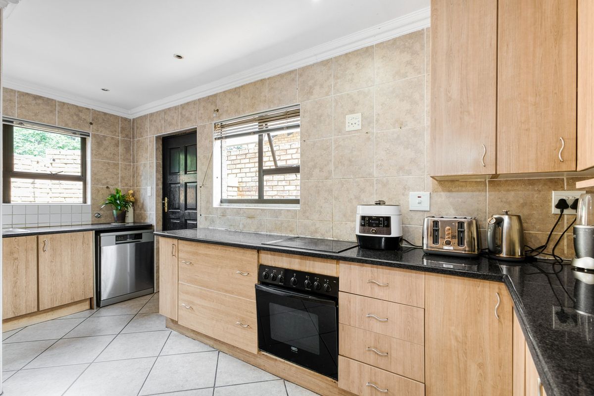A functional kitchen featuring light wood cabinetry, dark granite countertops, a built-in oven and hob, and neutral tiled finishes throughout.