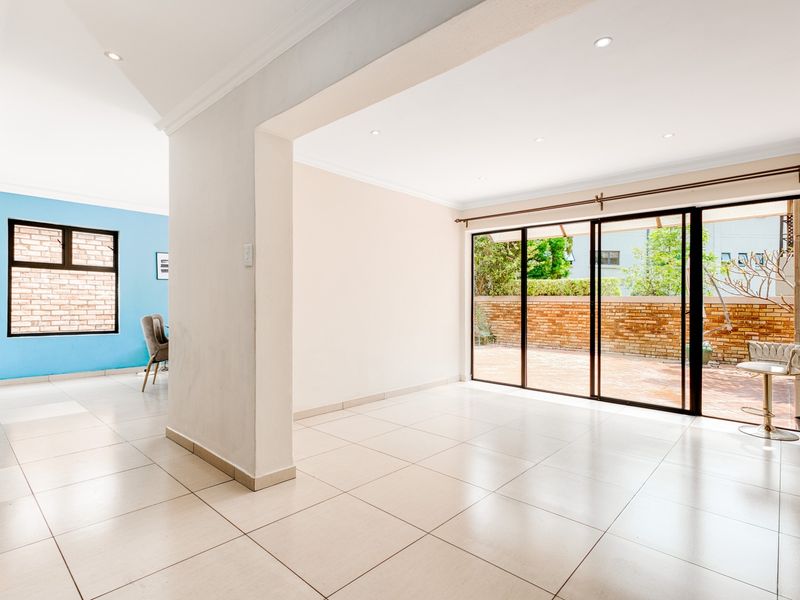 Spacious open-plan living area featuring neutral tiled flooring, recessed downlights, and large sliding glass doors providing seamless access to the outdoor patio.