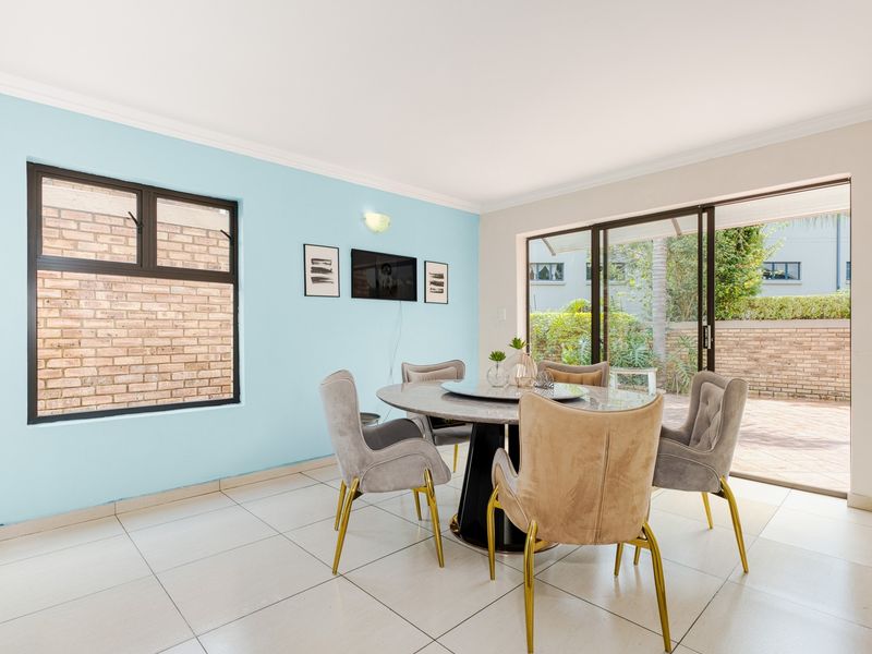Bright dining area featuring tiled flooring, aluminium window frames, and large sliding glass doors providing direct access to the outdoor patio.