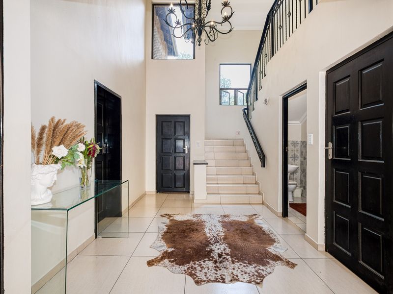 Spacious double-volume entrance hall featuring tiled flooring, a wrought iron staircase, and access to multiple rooms.