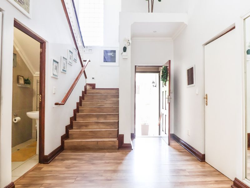 Bright and welcoming entrance hall featuring a wooden staircase, laminate flooring, and direct access to a guest bathroom.