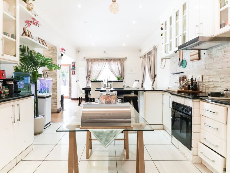 Spacious open-plan kitchen and dining area featuring white cabinetry, stone tile flooring, and a modern stone-clad backsplash.