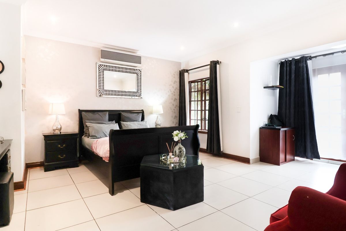 Spacious bedroom featuring tiled flooring, a wall-mounted air conditioning unit, and direct access to an outdoor area through glass french doors.