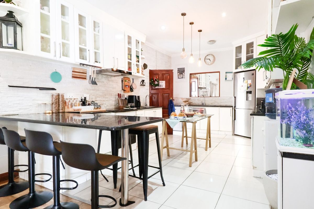 A bright, well-maintained kitchen featuring white cabinetry, granite countertops, tiled flooring, and modern pendant lighting, offering a functional and clean culinary space.
