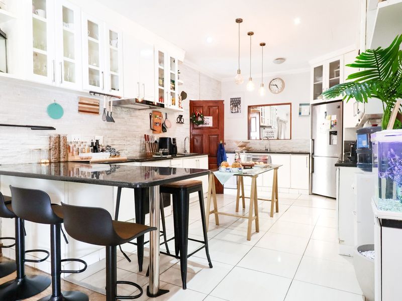 A bright, well-maintained kitchen featuring white cabinetry, granite countertops, tiled flooring, and modern pendant lighting, offering a functional and clean culinary space.