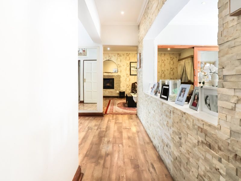 A bright hallway featuring a textured stone cladding wall, laminate flooring, and recessed lighting, leading into an adjacent living area with a fireplace.