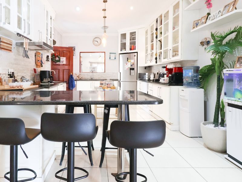 A bright, well-maintained kitchen featuring white cabinetry, granite countertops, tiled flooring, and a central breakfast bar with integrated lighting.