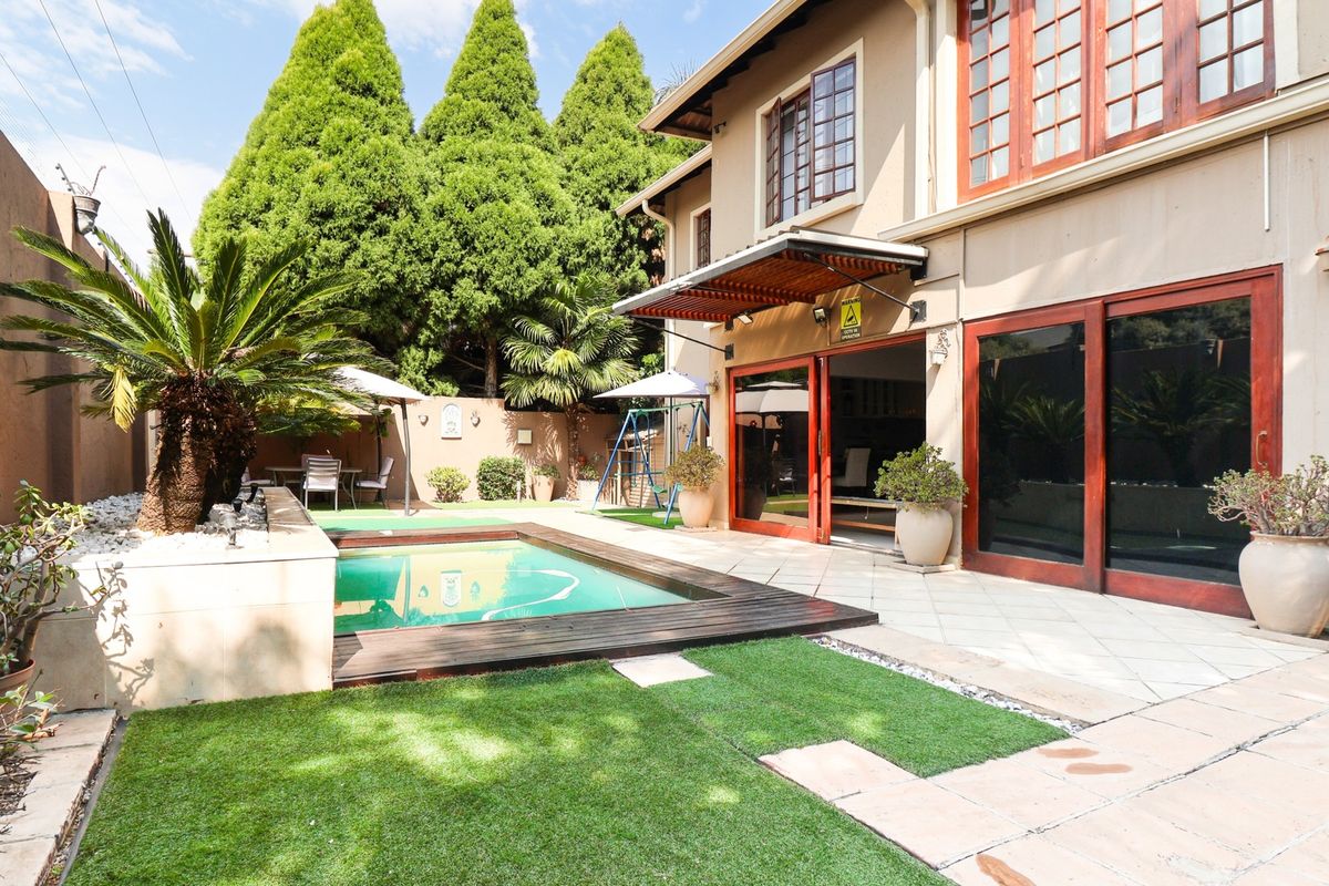 Rear exterior view featuring a swimming pool with timber decking, a tiled patio area, and sliding glass doors leading into the home.