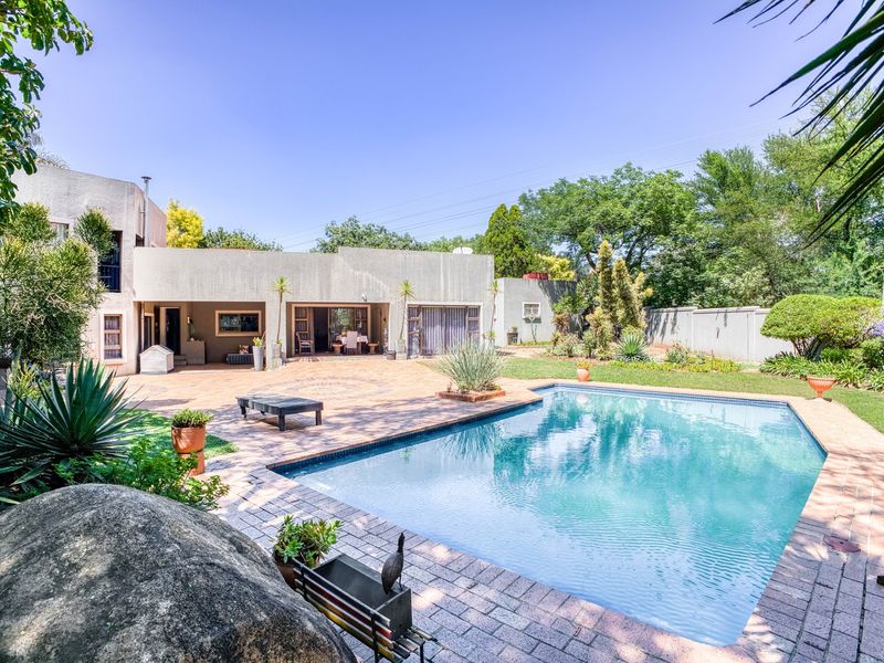 Spacious rear garden featuring a large swimming pool, extensive brick-paved patio area, and a covered outdoor entertainment space.