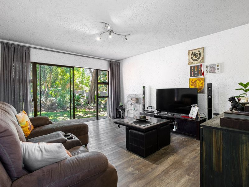 A comfortable living room featuring laminate flooring, textured walls, and large sliding glass doors that provide direct access to the garden.