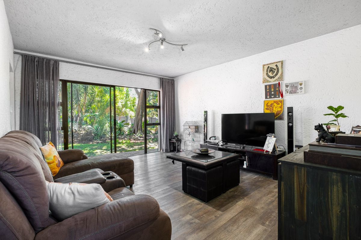 A comfortable living room featuring laminate flooring, textured walls, and large sliding glass doors that provide direct access to the garden.