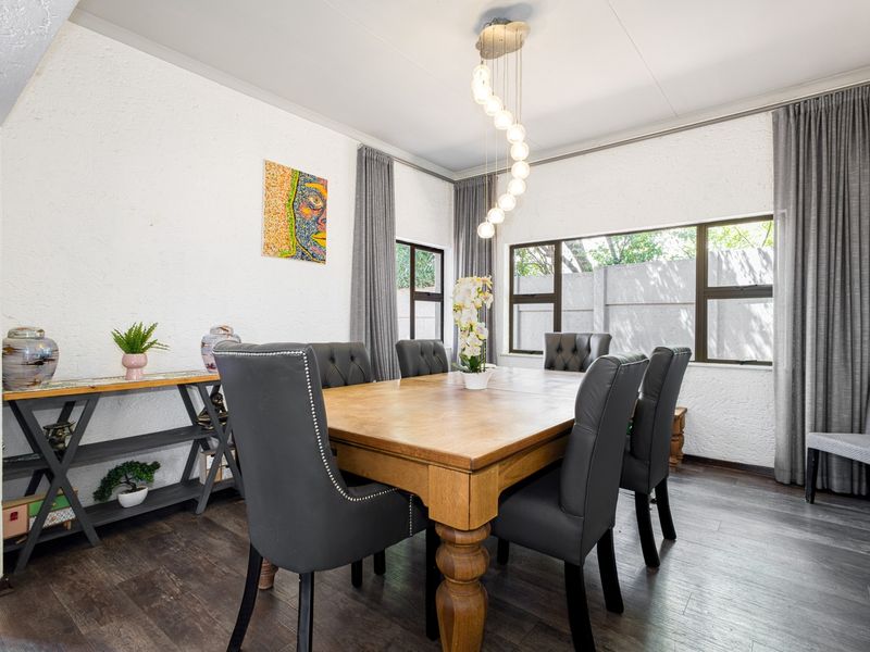 A well-lit dining room featuring textured walls, dark laminate flooring, and large windows with integrated curtain tracks, creating a comfortable and functional space.