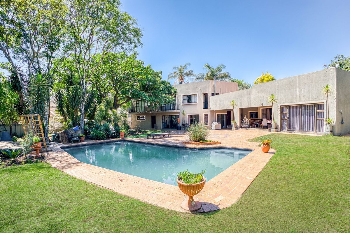 Spacious rear exterior featuring a swimming pool, brick-paved patio area, established garden, and a multi-level house facade with a balcony.