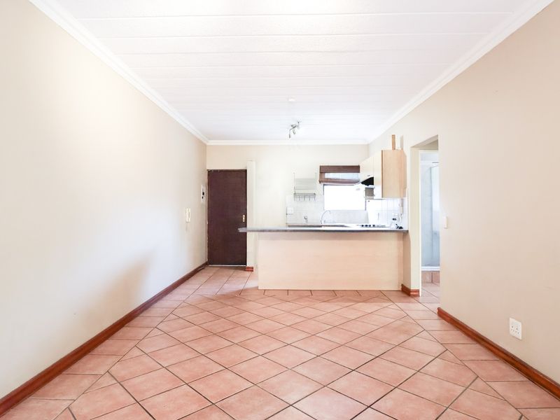 An open-plan living and kitchen area featuring tiled flooring, neutral walls, and functional kitchen cabinetry with a breakfast counter.