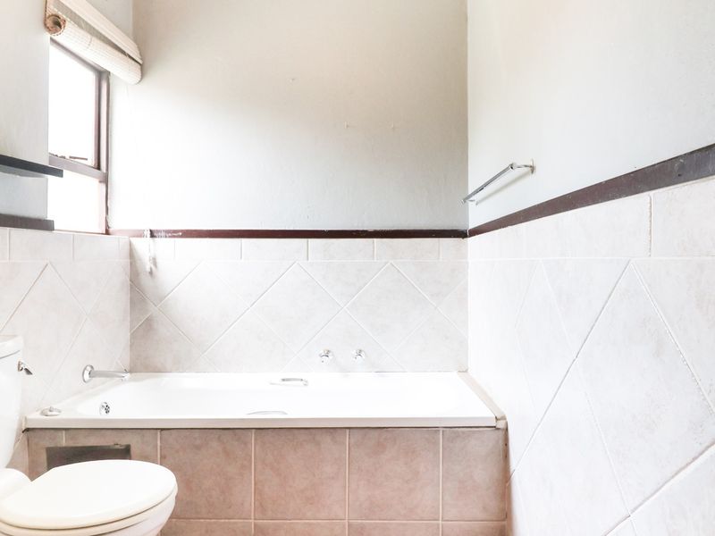 A functional bathroom featuring a built-in bathtub, toilet, and tiled wall finishes, offering a clean space ready for potential cosmetic updates.