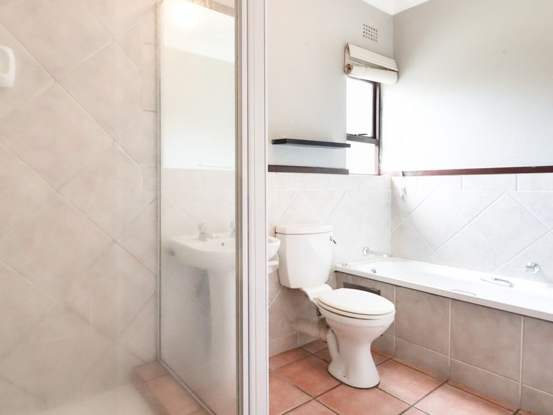 A functional bathroom featuring a shower enclosure, pedestal basin, toilet, and bathtub with neutral wall and floor tiling.