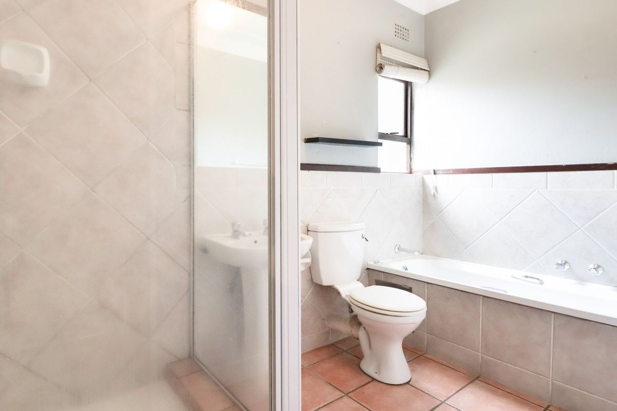 A functional bathroom featuring a shower enclosure, pedestal basin, toilet, and bathtub with neutral wall and floor tiling.
