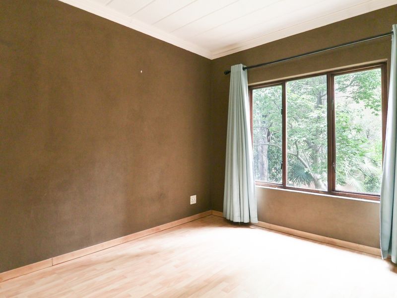 An empty bedroom featuring laminate flooring, dark painted walls, and a large window with garden views.