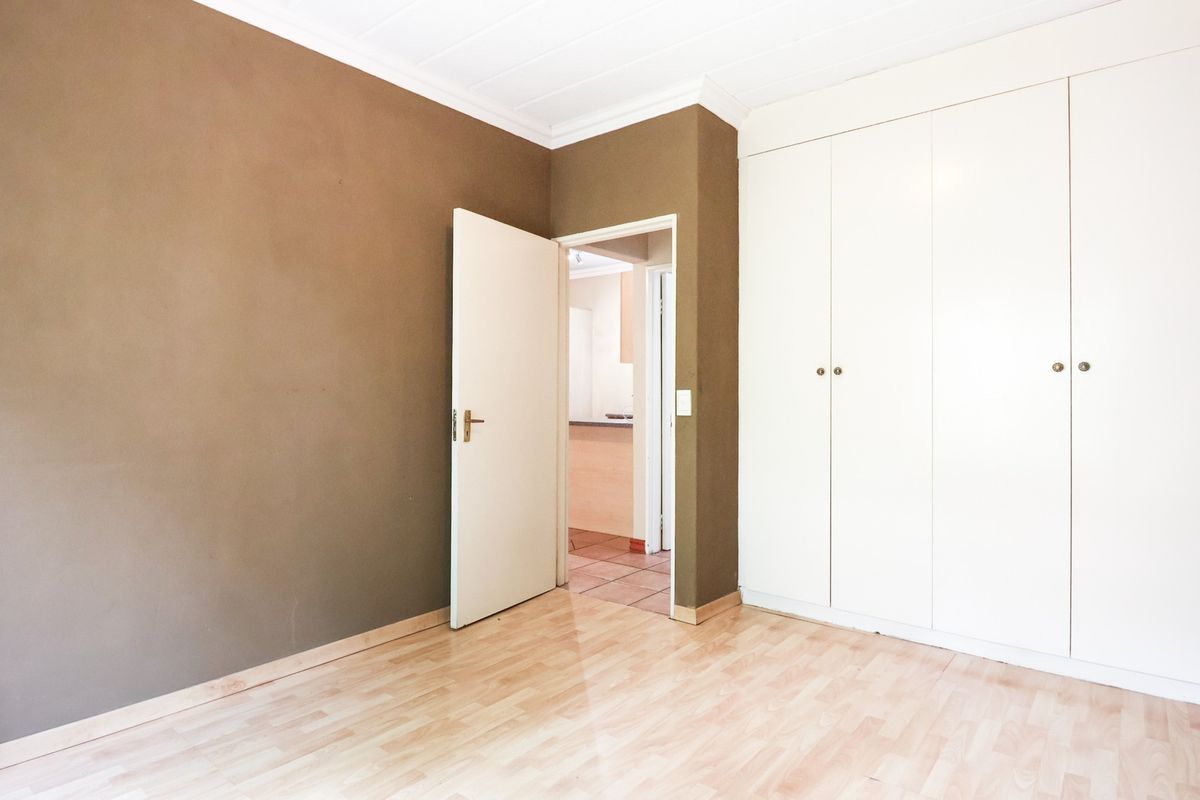 An empty bedroom featuring laminate flooring, built-in cupboards, and neutral wall finishes, offering a blank canvas for personalization.