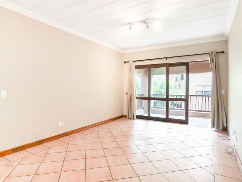 An empty living room featuring tiled flooring, a sliding glass door leading to a balcony, and a paneled ceiling.