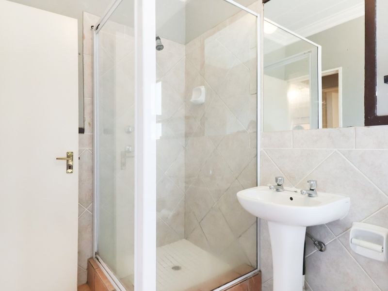A functional bathroom featuring a glass shower enclosure, pedestal basin, toilet, and neutral wall tiling.