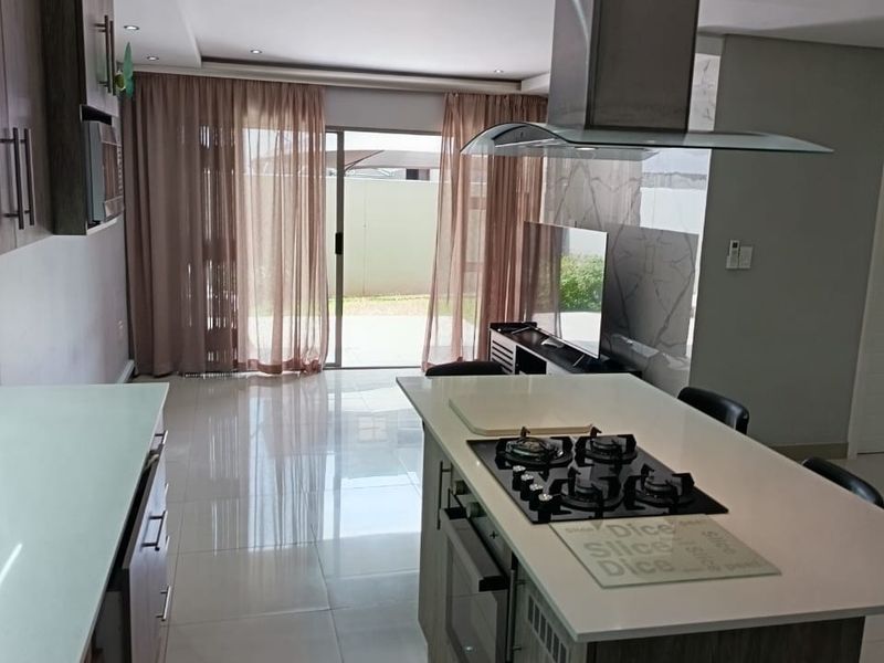 Modern open-plan kitchen featuring a central island with gas hob, built-in oven, and extractor fan, flowing seamlessly into the living area with sliding door access.