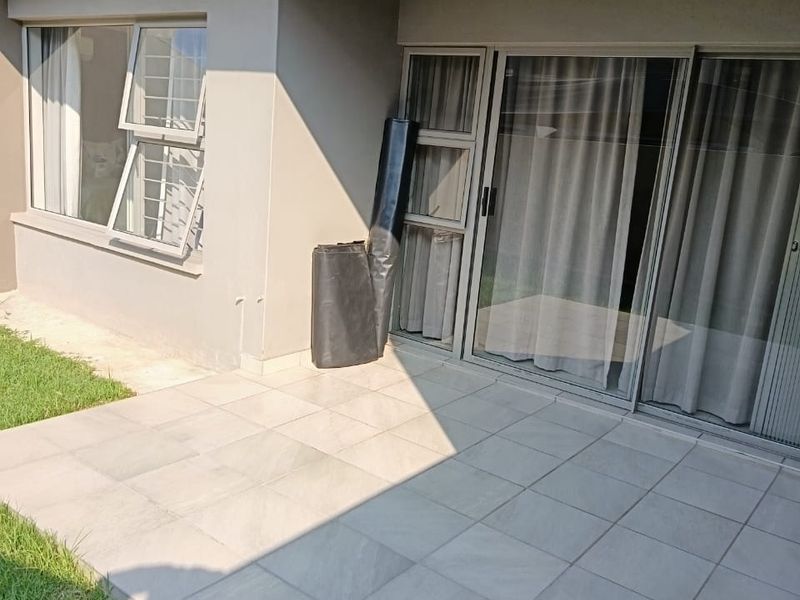 A clean, tiled patio area featuring sliding glass doors and aluminium window frames, providing direct access to the apartment interior.
