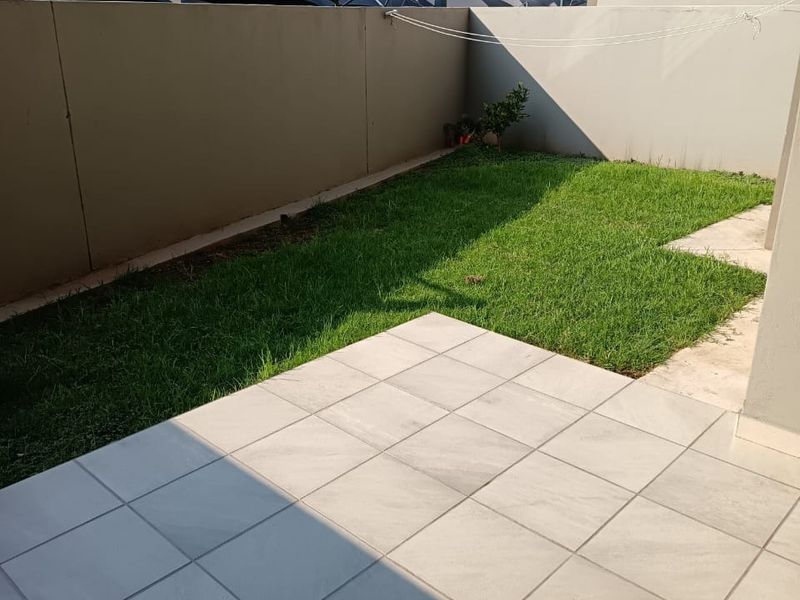 A private rear garden featuring a paved patio area, a small lawn, and high boundary walls for privacy.